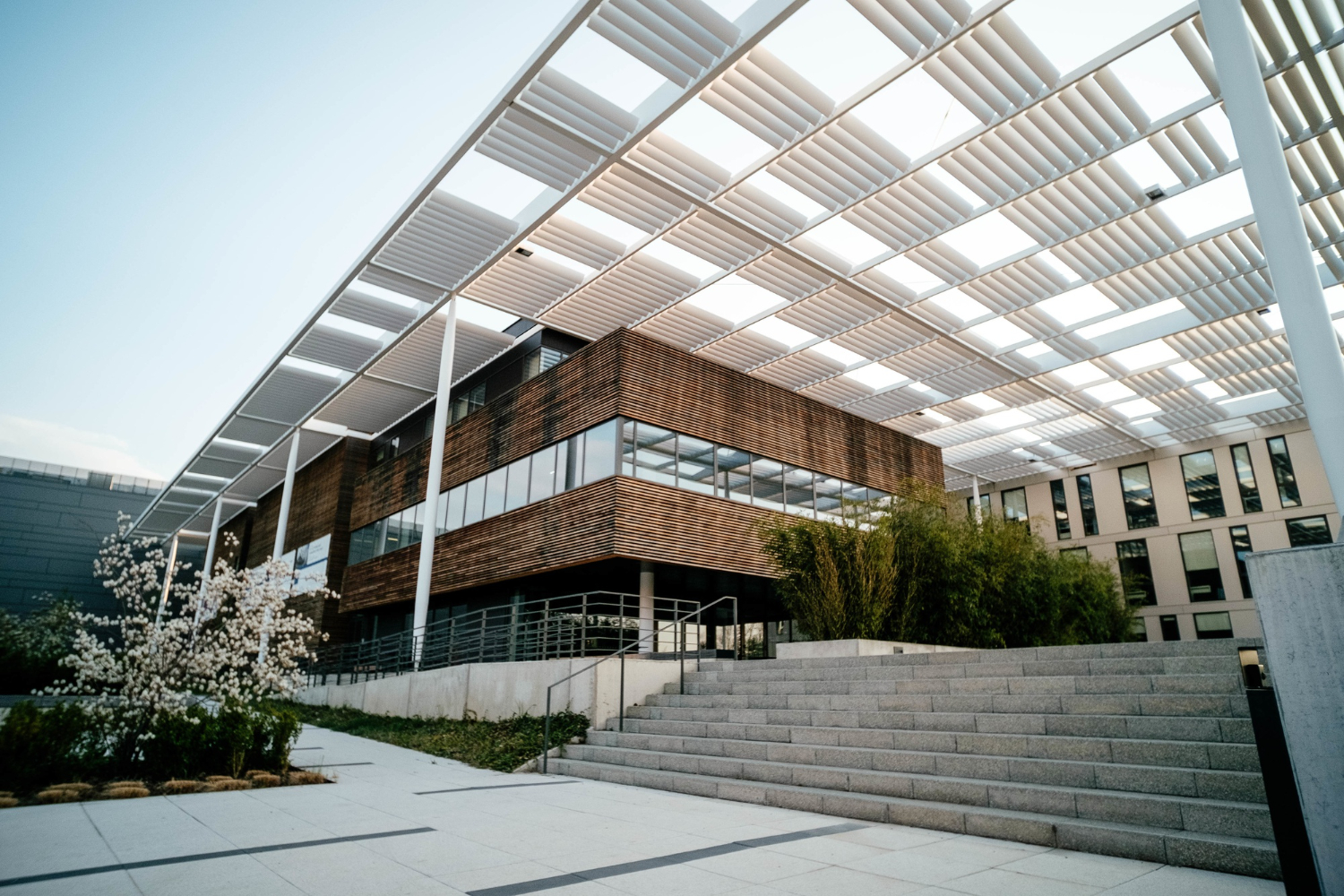 Bâtiment de bureaux moderne opusbati à Toulouse avec façade bois et verre, pergola blanche et escalier entouré de verdure