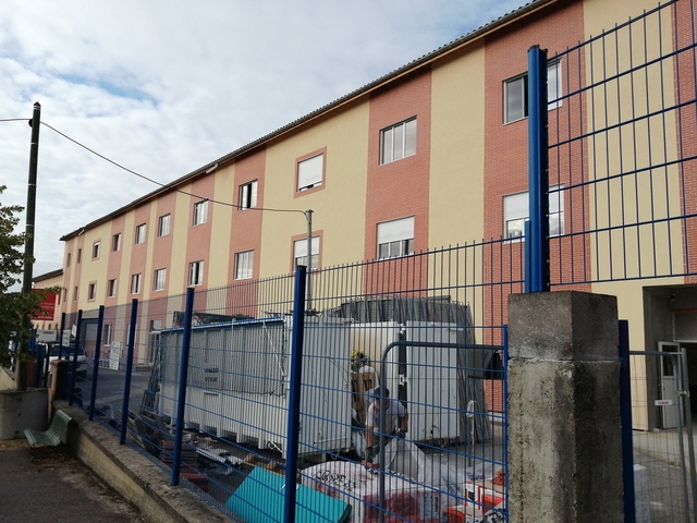 Chantier de rénovation d’immeuble opusbati à Toulouse avec clôture bleue, conteneurs blancs et ouvriers