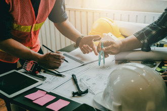 Plans de chantier étudiés par deux collaborateurs opusbati à Toulouse avec outils et casques de sécurité